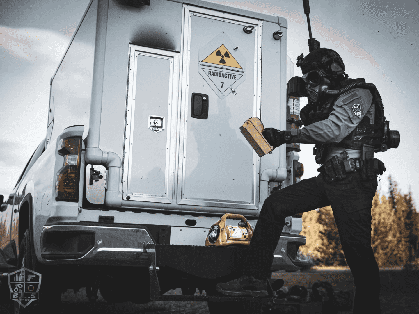 Responder in a respirator beside a pickup truck marked with a radioactive placard