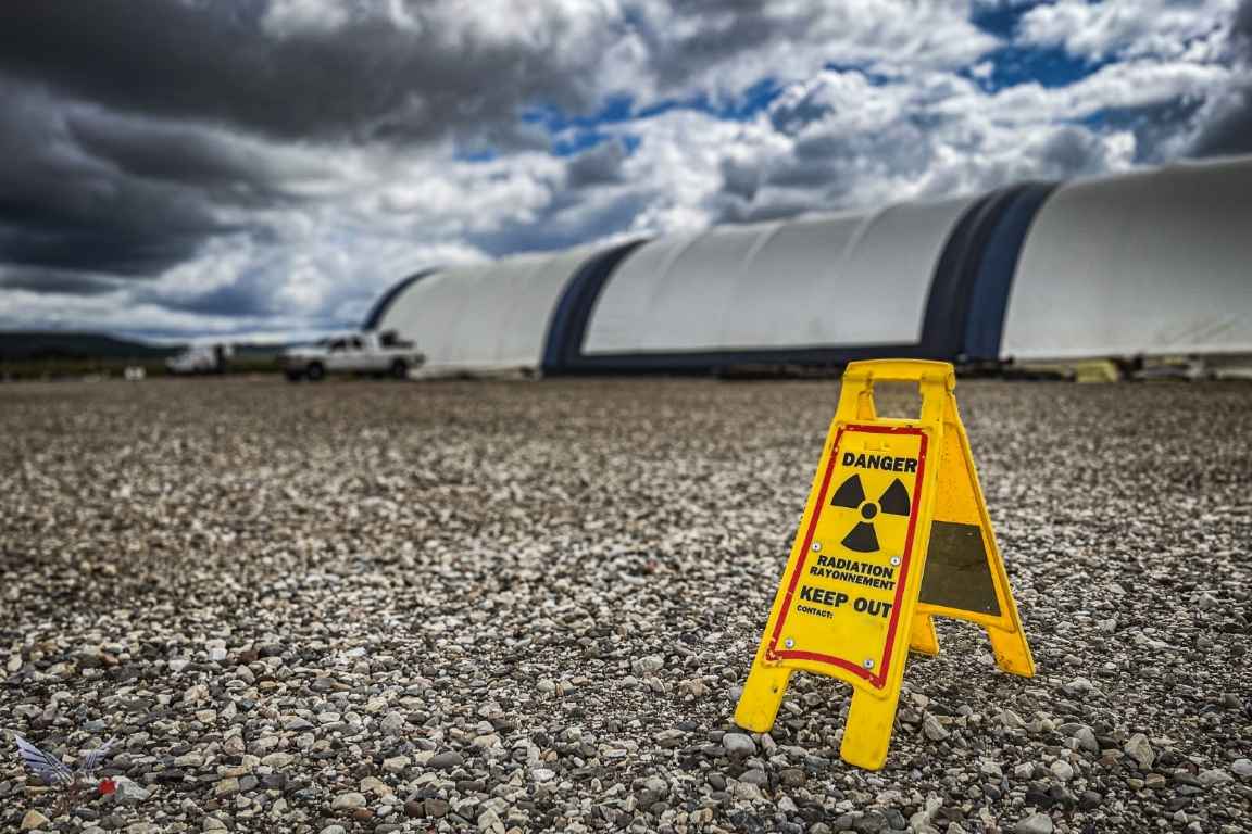Yellow radiation warning sign standing on gravel outside a dome building